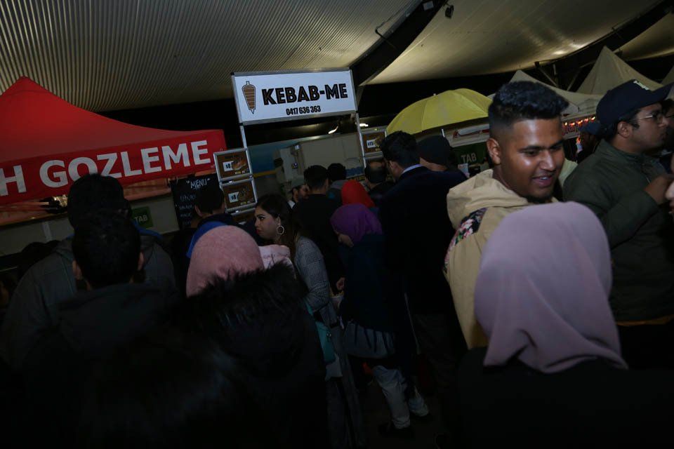 A crowd of people are standing in front of a kebab me stand
