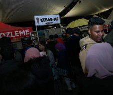 A group of people are standing in front of a kebab me stand.