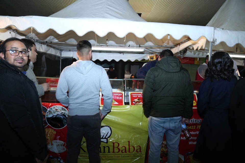 A group of people standing in front of a food stand called khan baba