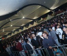 A large crowd of people are gathered in a stadium behind a fence.