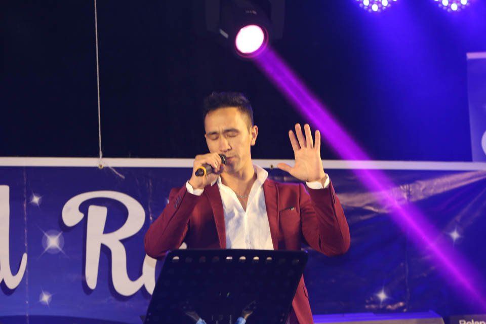 A man in a red jacket is singing into a microphone on a stage.