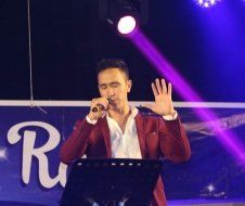 A man in a red jacket is singing into a microphone on a stage.