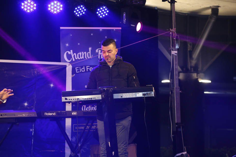 A man is playing a keyboard on stage in front of a banner that says chand