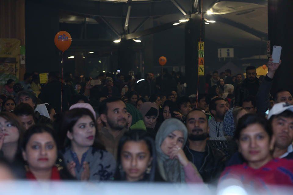 A crowd of people sitting in a dark room with an orange balloon hanging from the ceiling