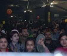 A large group of people are sitting in a room with balloons in the background.
