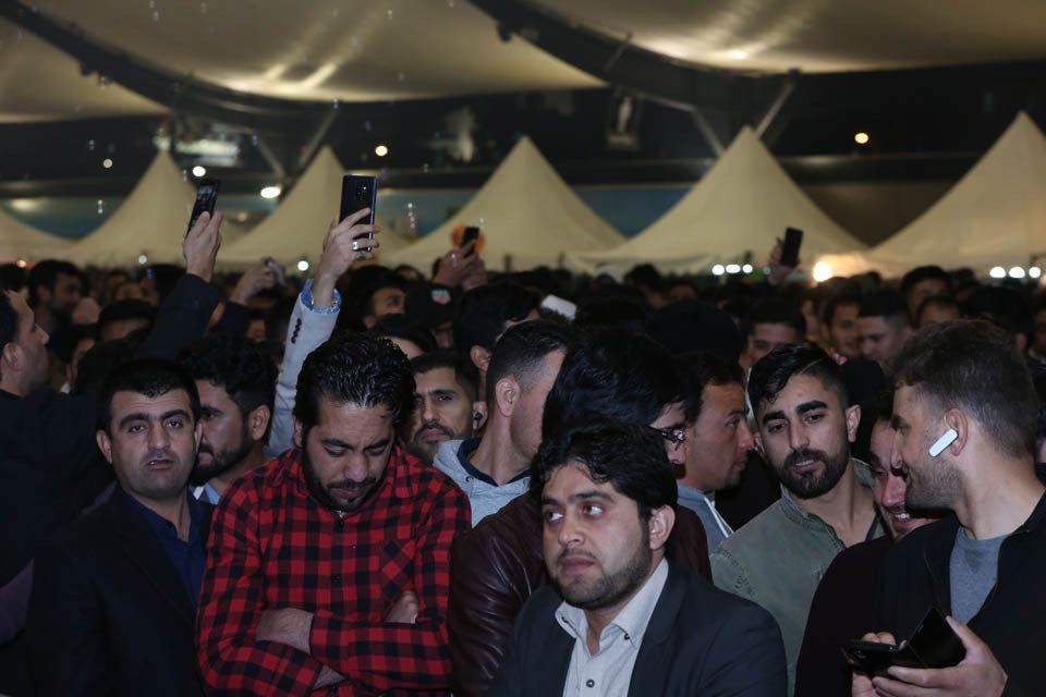 A group of men are sitting in a room with tents in the background.