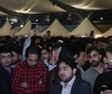 A crowd of people are sitting in a room with tents in the background.