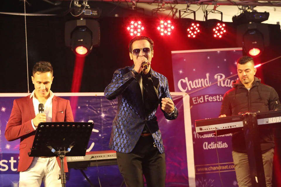 A man is singing into a microphone while two other men play keyboards.