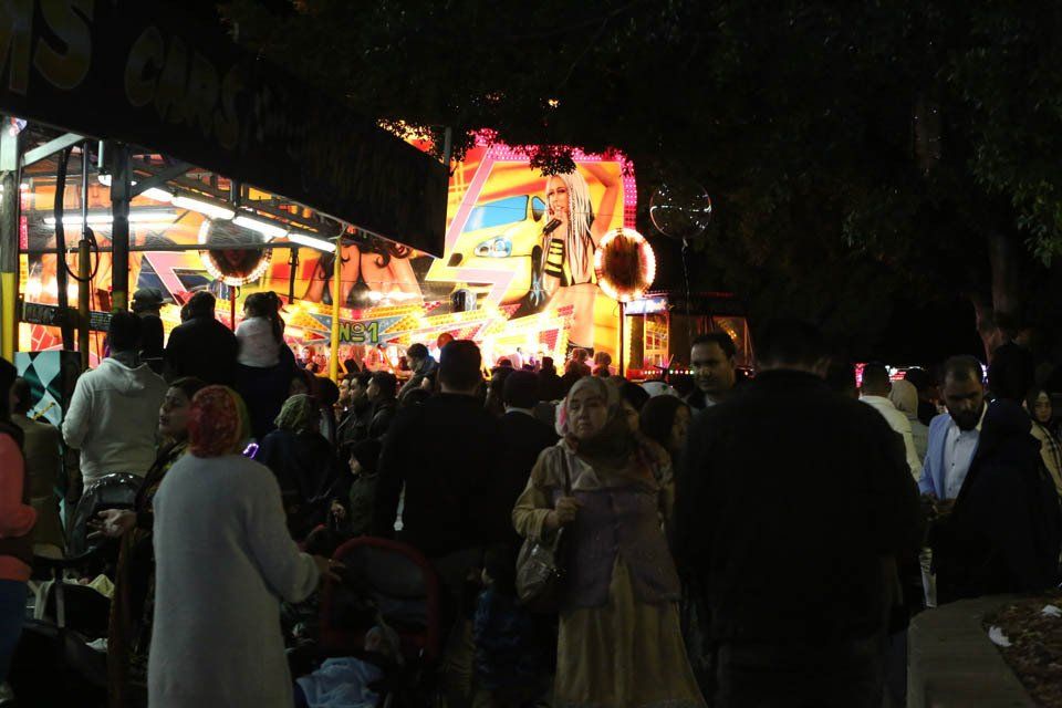 A crowd of people are standing in front of a carnival ride at night.