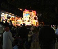 A crowd of people are standing in front of a carnival ride at night.