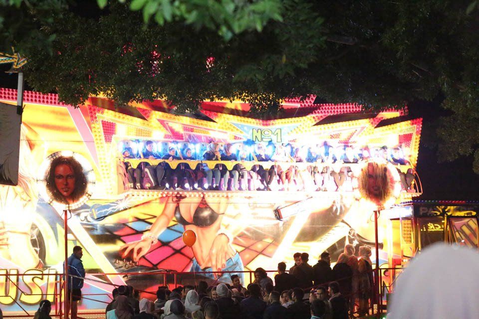 A crowd of people are gathered in front of a carnival ride