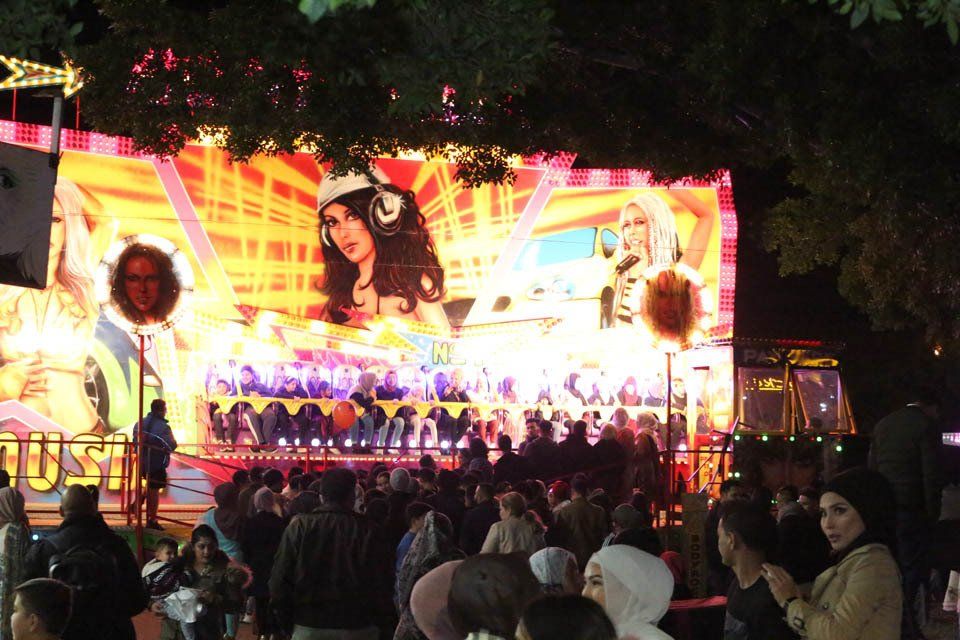 A crowd of people are gathered in front of a large screen with a woman on it