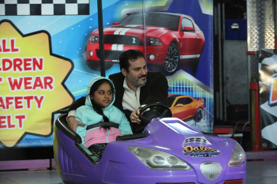 A man and two children are riding in a purple toy car