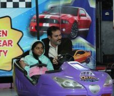 A man and a little girl are riding a purple toy car.