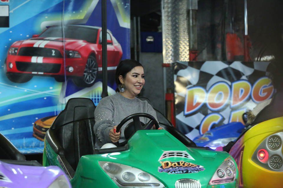 A woman is sitting in a green bumper car at an amusement park.
