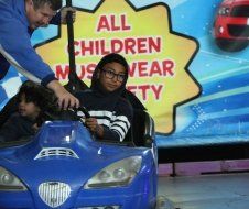 A man is pushing a child in a blue car in front of a sign that says 