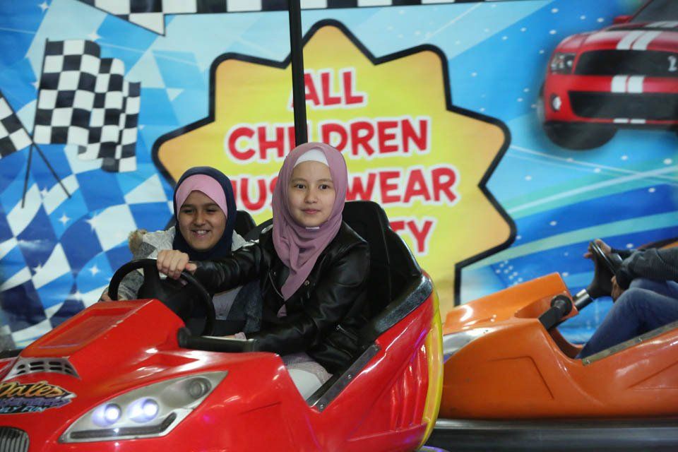 Two girls are riding a bumper car in front of a sign that says 