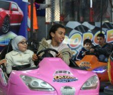 A woman and two children are riding a pink bumper car.
