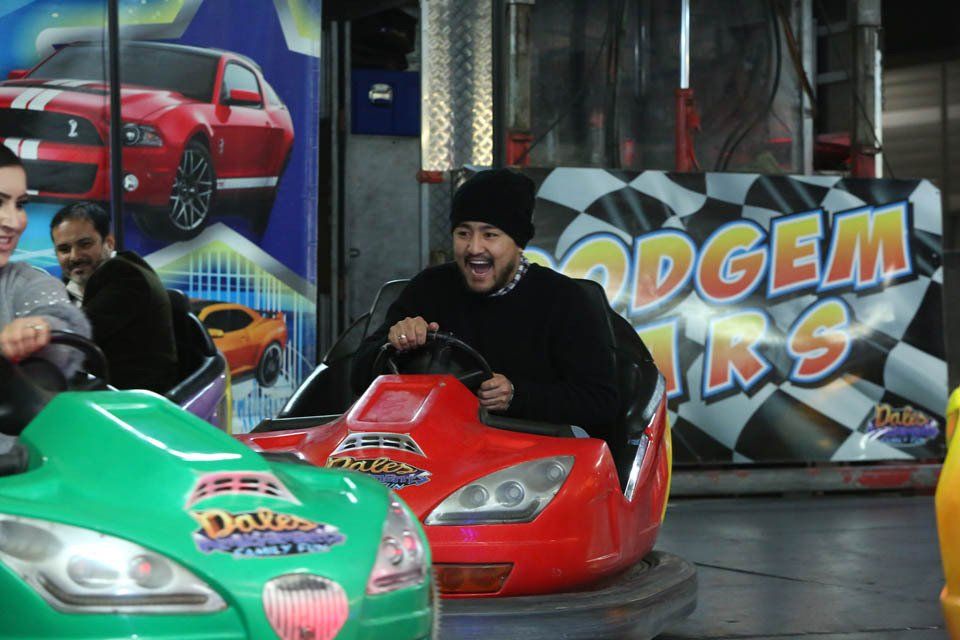 A man laughs while riding a bumper car in front of a sign that says odgem tracks