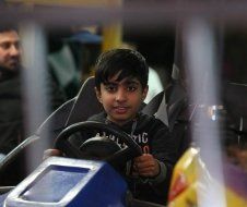 A young boy is driving a go kart in an amusement park.