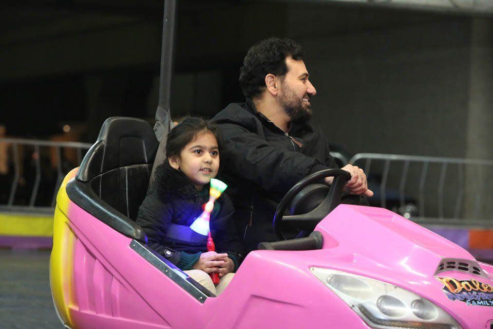 A man and a little girl are riding a pink bumper car.
