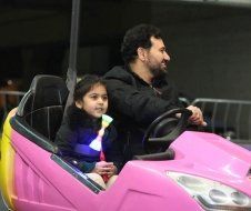 A man and a little girl are riding a pink bumper car.