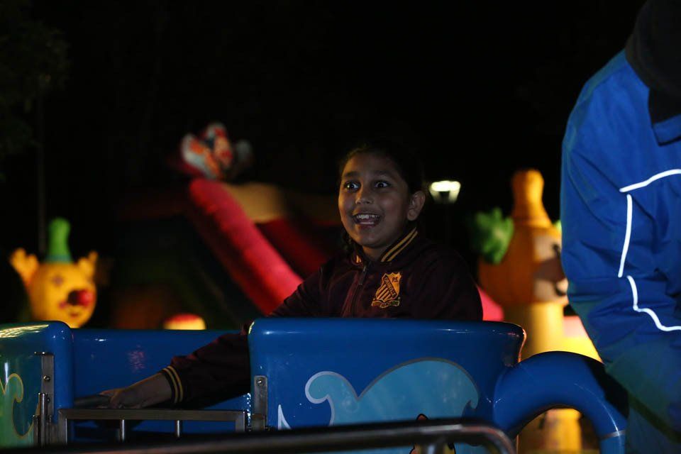 A little girl is riding a roller coaster at night.