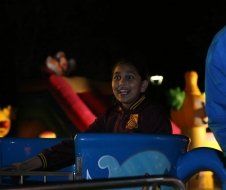 A young girl is riding a blue cup ride at night.