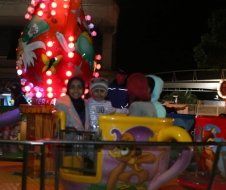 A group of people are riding a teacup ride in front of a christmas tree.