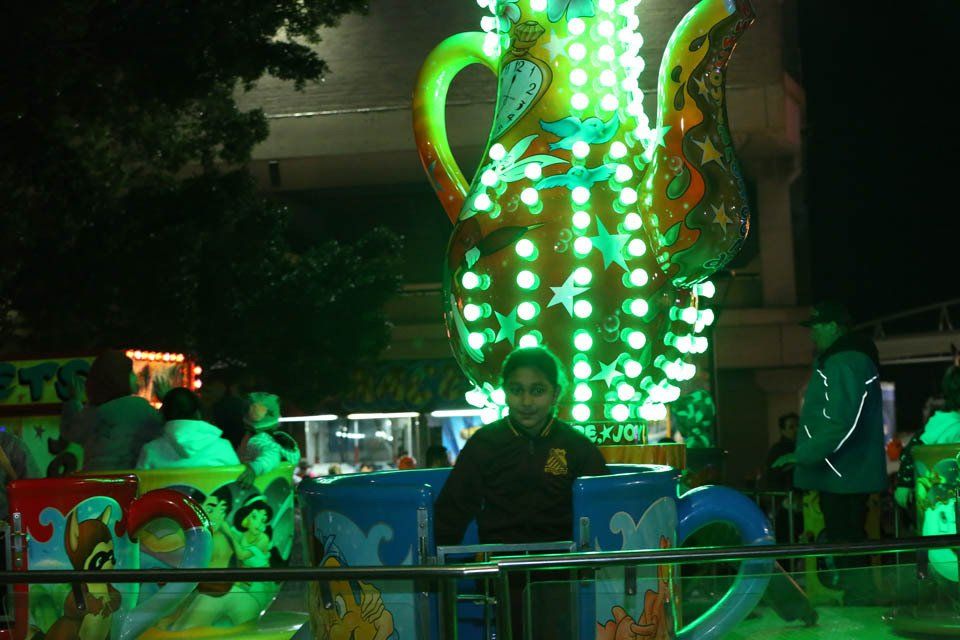 A man is standing in front of a large teapot with green lights on it.