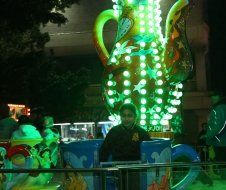 A man is standing in front of a giant teapot that is lit up at night.