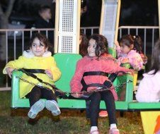 Three little girls are sitting on a green swing.