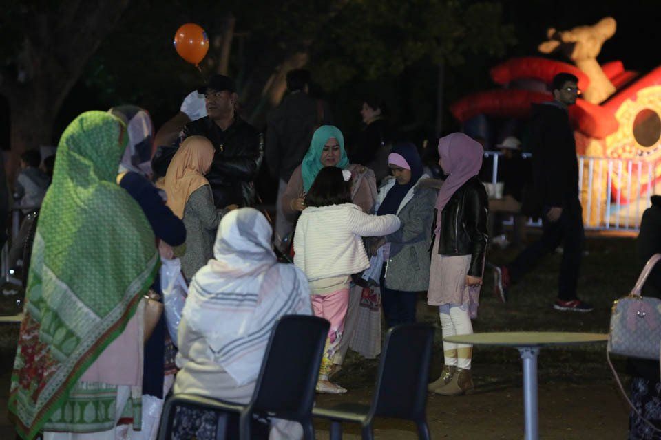 A group of people are gathered in a park at night.
