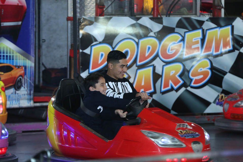 A man and a child are riding a bumper car in front of a sign that says dodge cars