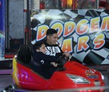 A man and a boy are riding a bumper car at a carnival.