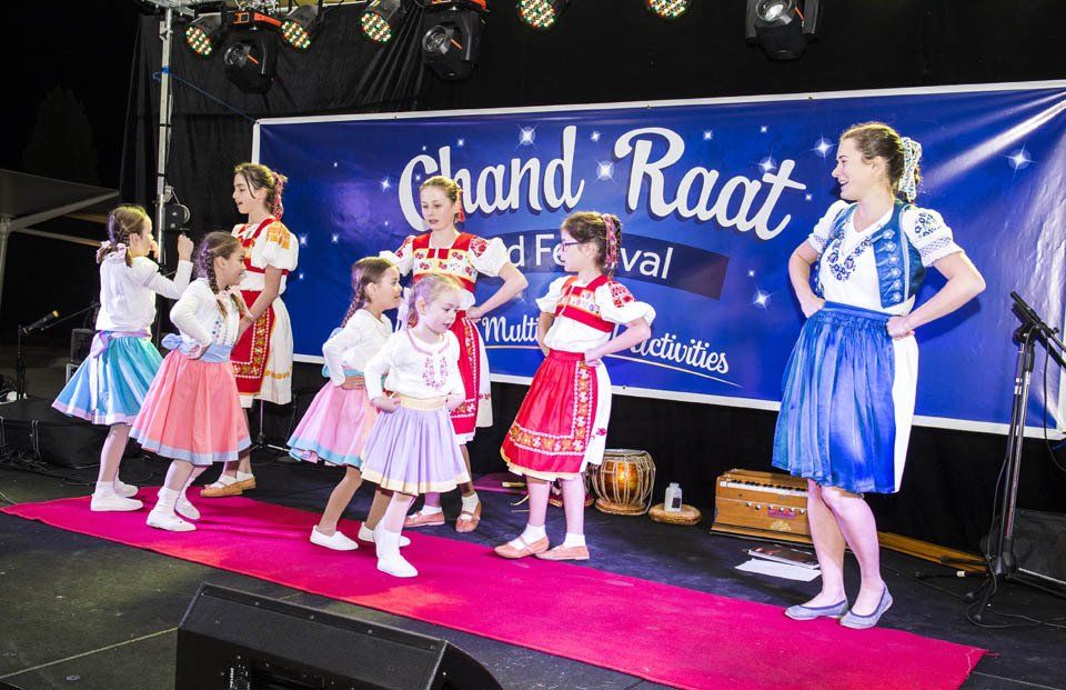 A group of young girls are dancing on a stage in front of a sign that says grand raat.