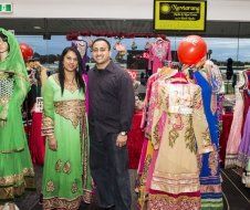 A man and a woman are posing for a picture in front of a display of dresses.