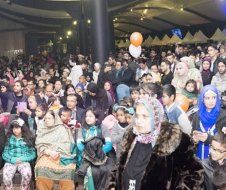 A large group of people are sitting in a room with balloons.
