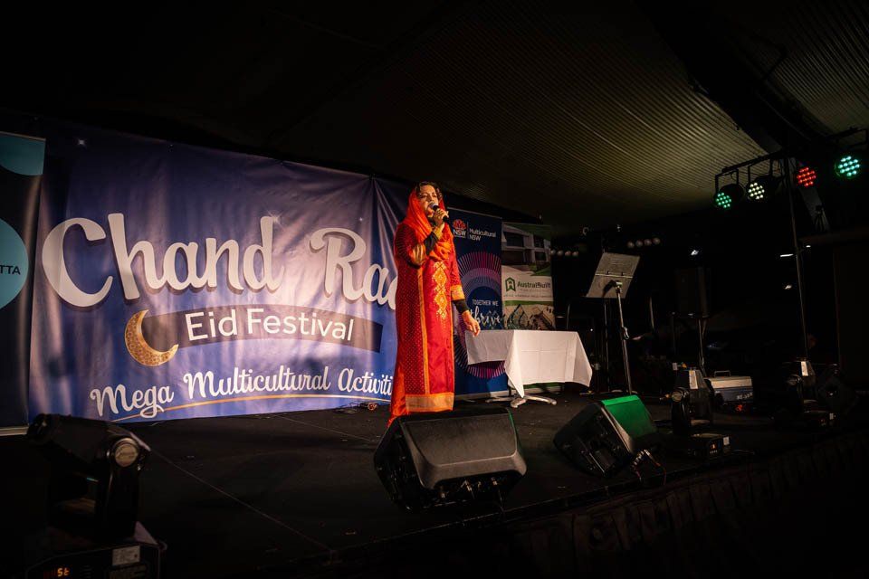 A woman is singing into a microphone on a stage in front of a banner.