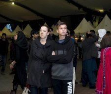 A man and a woman are standing in a crowd with their arms crossed.