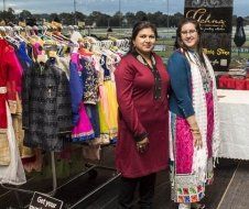 Two women are standing next to each other in front of a clothing rack.