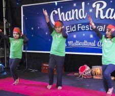 A group of children are dancing in front of a sign that says chand ram eid festival.