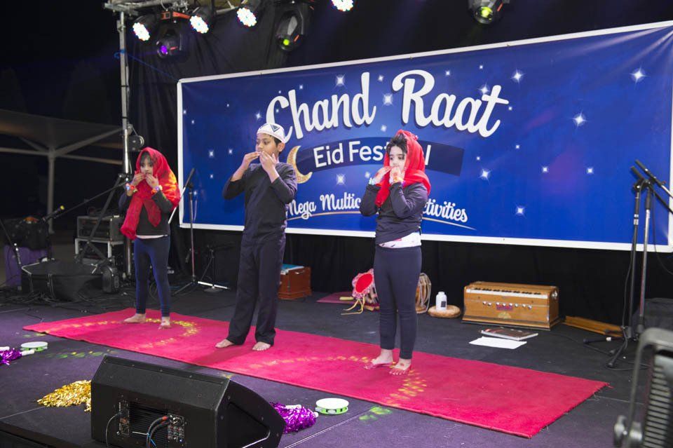 A group of people are standing on a stage in front of a banner that says chand raat