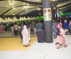 A crowd of people are gathered in a large room with a jar of coffee on the wall.