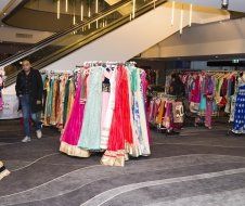 A man is walking through a store filled with lots of clothes.