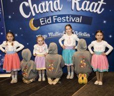 A group of young girls are posing for a picture in front of a sign that says chand raat eid festival.