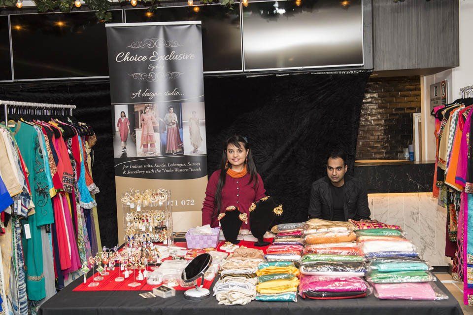 A woman and a man are standing behind a table with clothes on it.