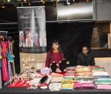 A woman is standing behind a table filled with clothes and jewelry.
