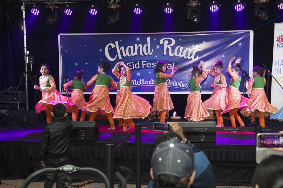 A group of people are dancing on a stage in front of a sign that says chand raat.