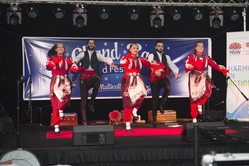 A group of people are dancing on a stage in front of a sign that says grand festival